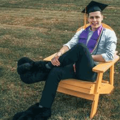 Caleb sitting on a campus chair wearing graduation cap and TC feet.