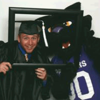 Drew Van Woert dressed for graduation and posing in a frame with TC