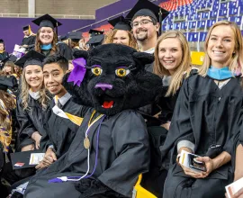 TK in gown while sitting in the bleachers with graduating students.